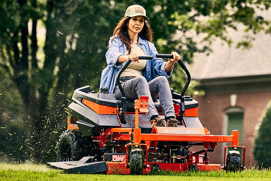 Person operating a riding lawn mower in a suburban setting MZ Rambler Residential Mower