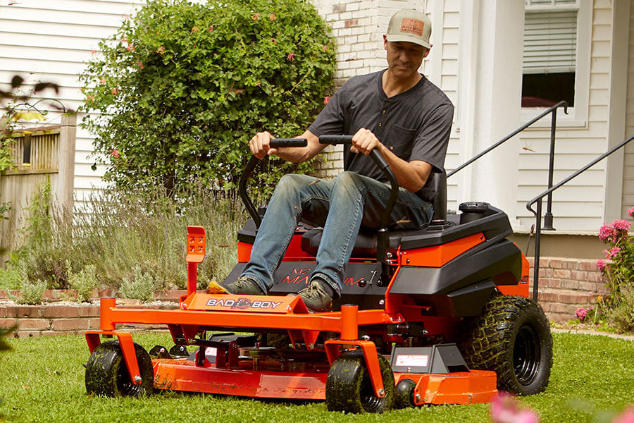 Man operating a riding lawn mower in a garden MZ Magnum Residential Lawn Mower